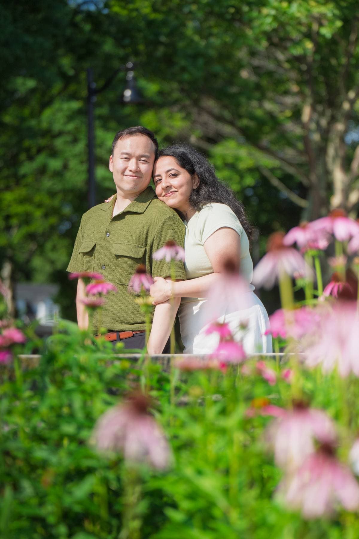 Sanjika and Andy embracing in a garden surrounded by pink coneflowers