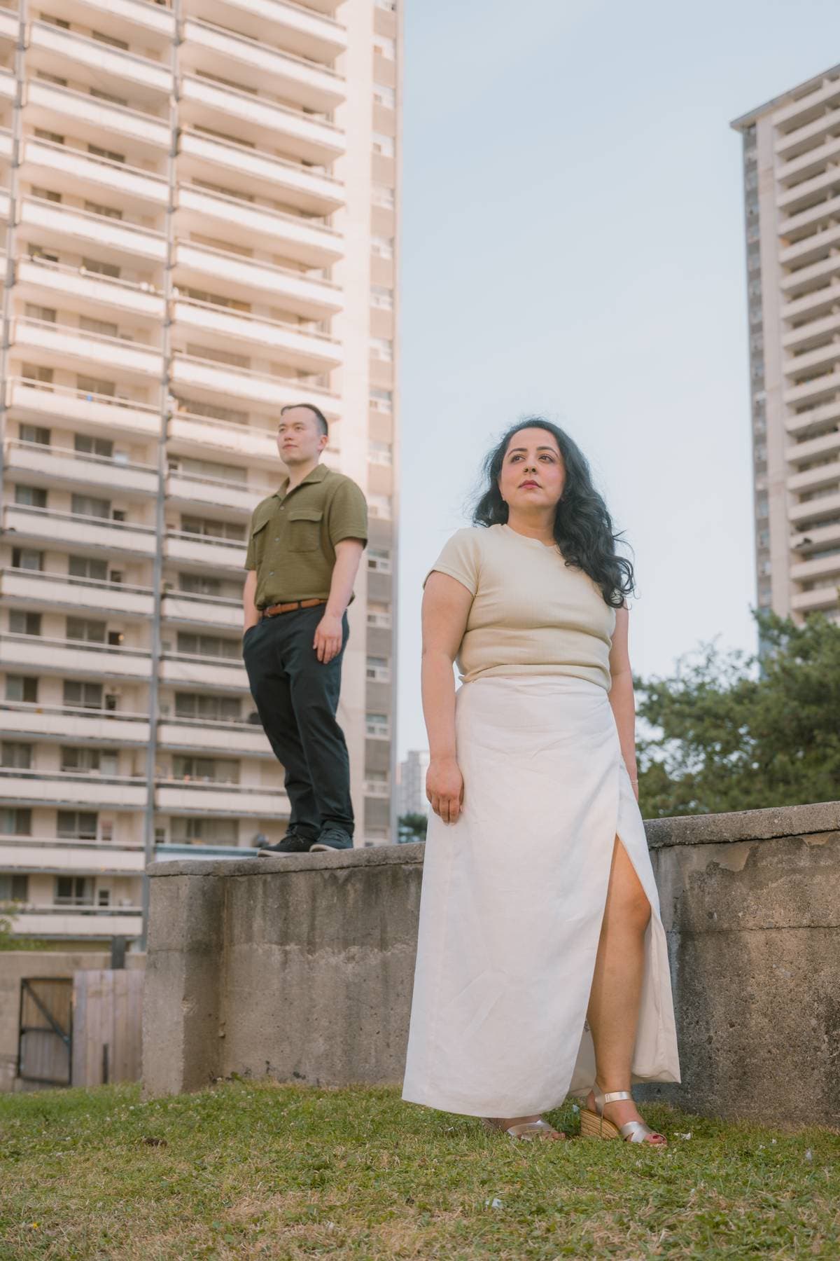 Sanjika and Andy standing apart on a rooftop ledge between two towers